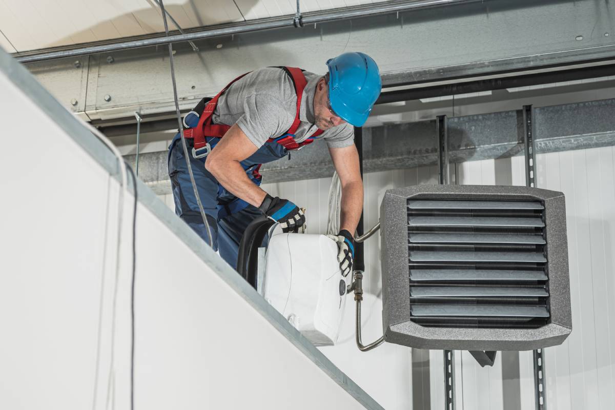 Caucasian HVAC Technician Worker in His 40s Installing Air and Water Heaters Inside Newly Constructed Warehouse.