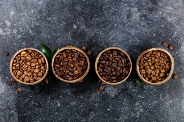Flat lay of Four different varieties of coffee beans on dark marble background, copyspace