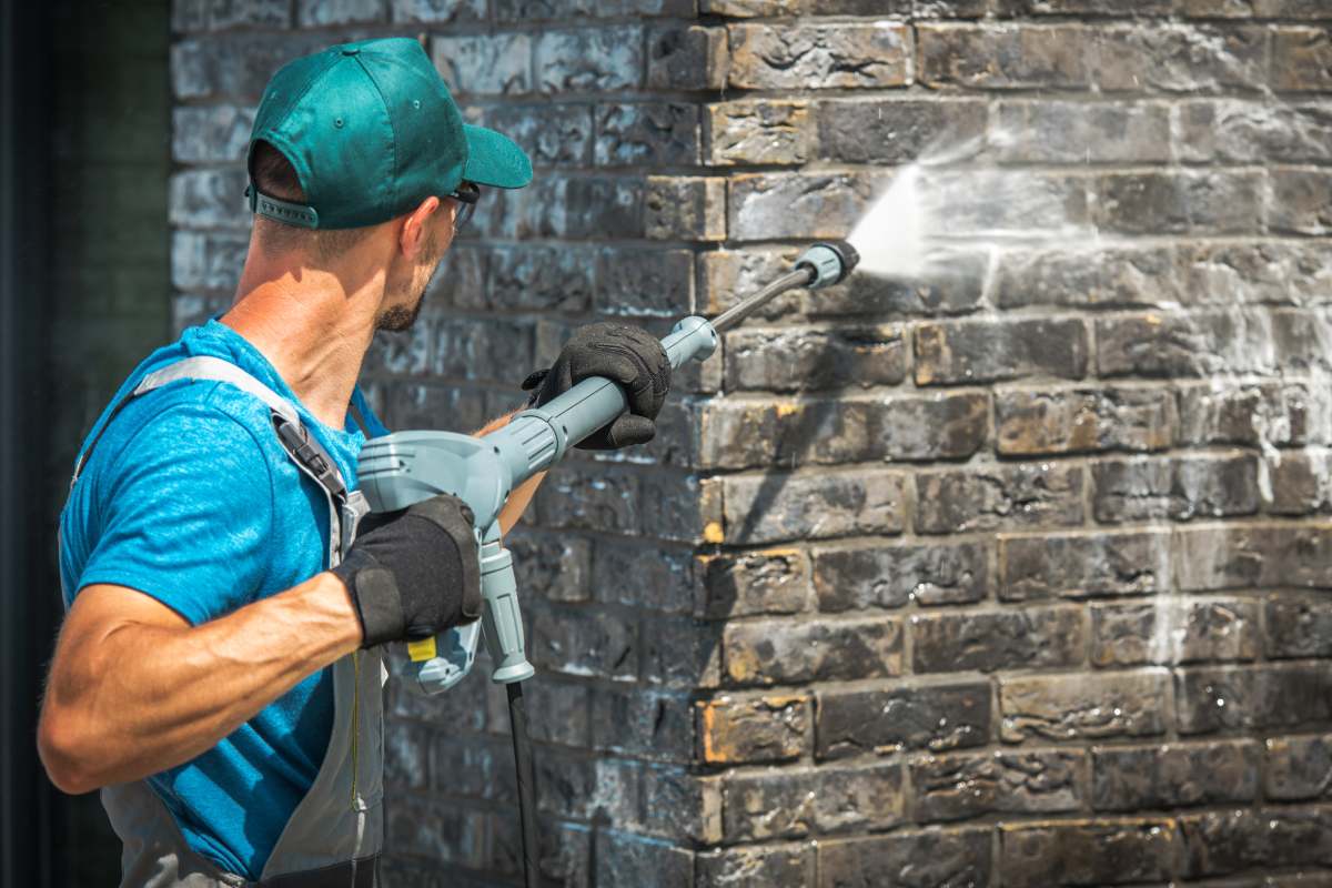 House Brick Wall Washing Using Pressure Washer. Caucasian Worker in His 30s.