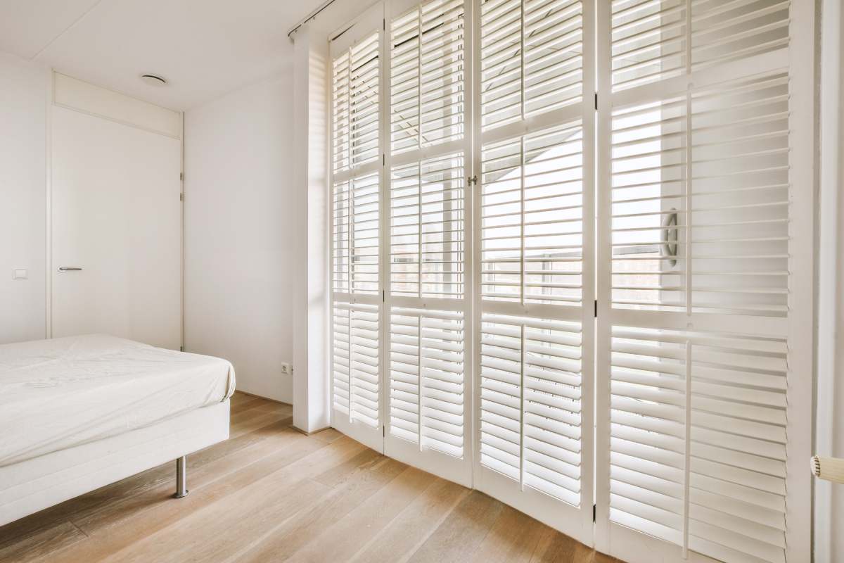 Home interior design of bedroom with bed and wooden wardrobe placed in corner near window in modern apartment